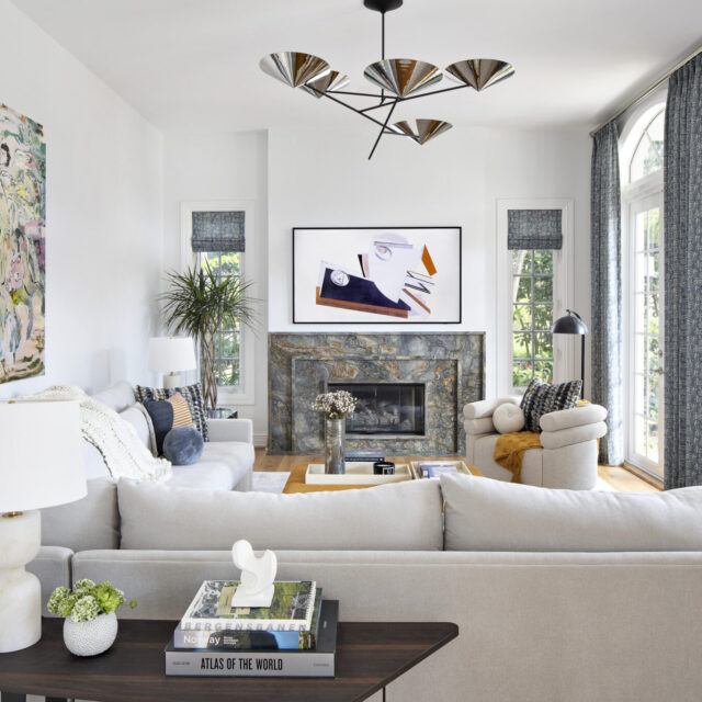 Modern South Florida living room with a dramatic stone fireplace, abstract artwork, sculptural chandelier, and layered seating in neutral tones.