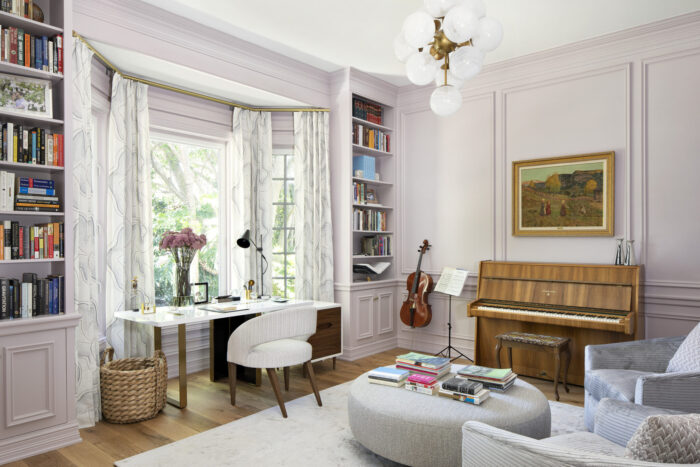 Elegant study featuring built-in bookshelves, a rounded ottoman, soft upholstered chair, and a globe chandelier, with a piano and cello adding warmth.