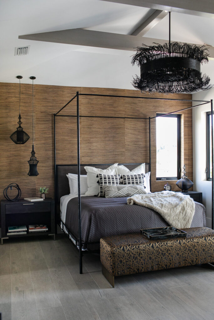 Master bedroom with seagrass wallpaper, antique iron four-poster bed by Oly Studio, and black opium pendants by Forestier Paris.