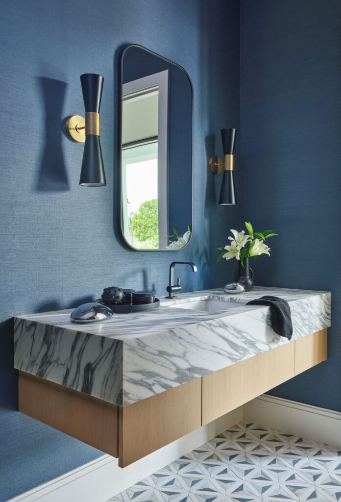 Modern Palm Beach powder room with blue textured walls, marble floating vanity, black and brass sconces, and fresh white lilies for contrast.