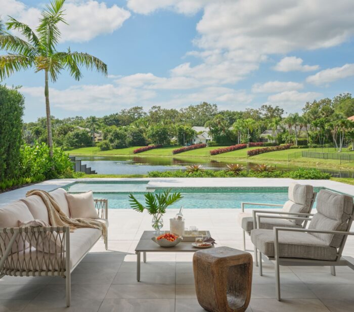 Outdoor living area in Palm Beach with modern seating, neutral tones, and a view of the pool and golf course surrounded by lush greenery and palm trees.