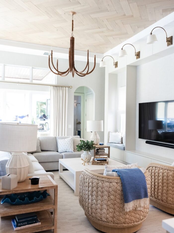 Bright coastal living room with woven swivel chairs, white sectional, natural textures, and light wood herringbone ceiling.