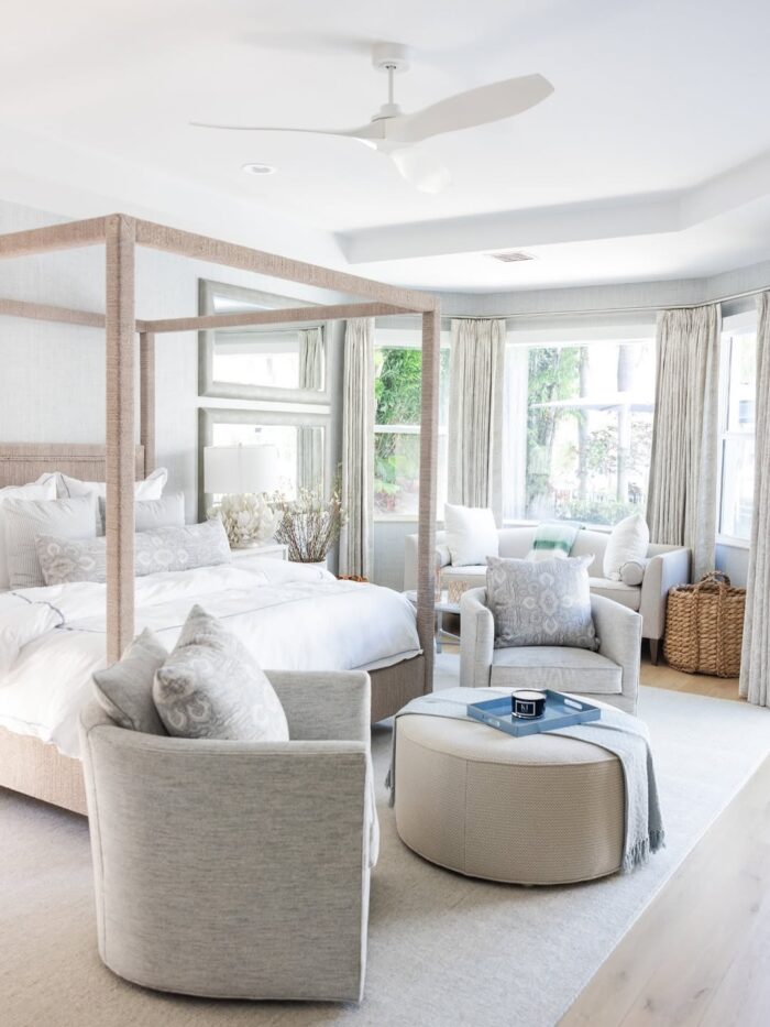 Serene primary bedroom with four-poster bed, neutral seating area, light drapery, and soft layered textures.