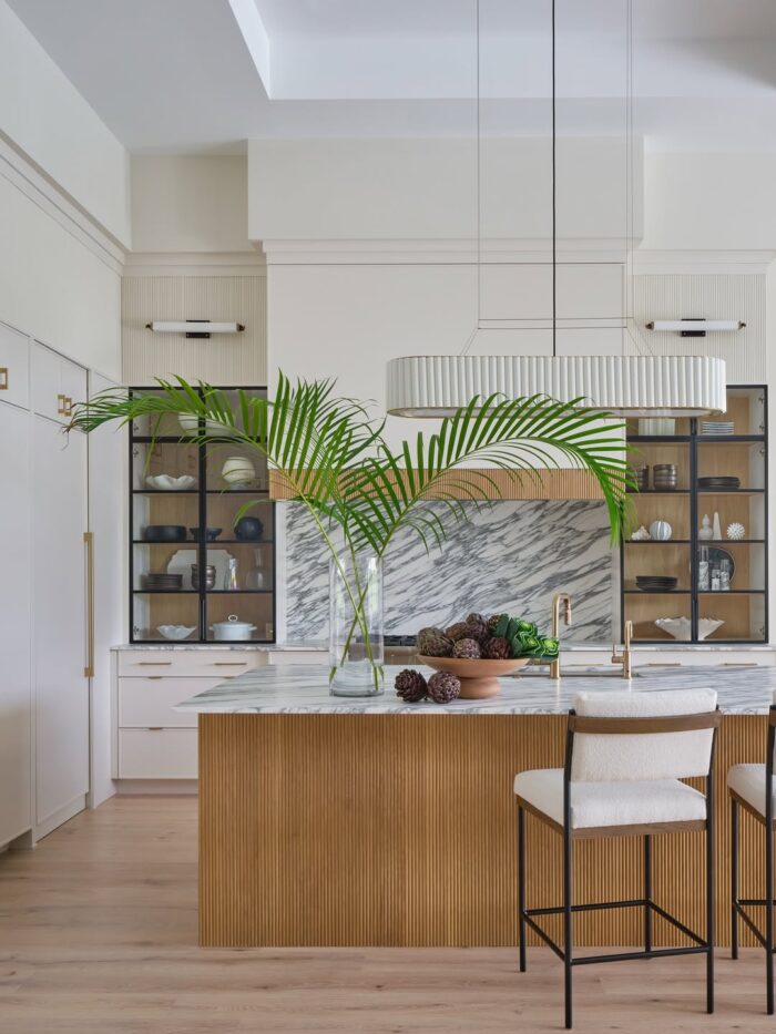 Palm Beach kitchen featuring a ribbed wood island, marble backsplash, glass-front cabinets, and tall palm fronds in a clear vase on the counter.