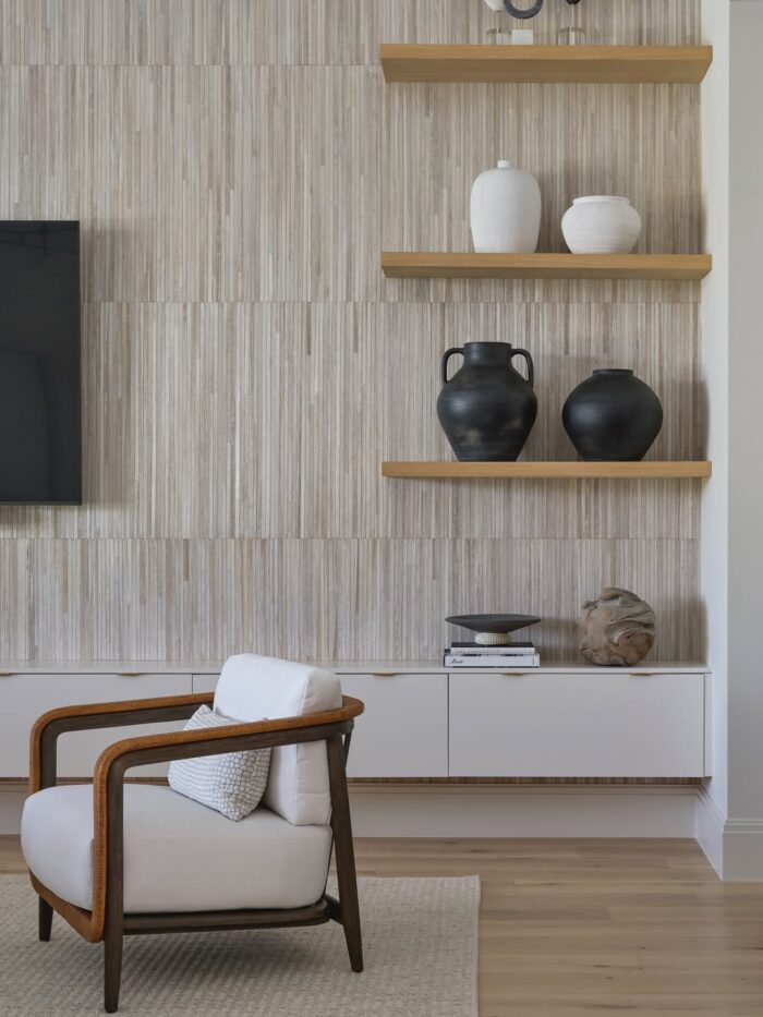 Textured living room wall with vertical paneling, floating wood shelves styled with black and white ceramics, and a modern wood-framed lounge chair.