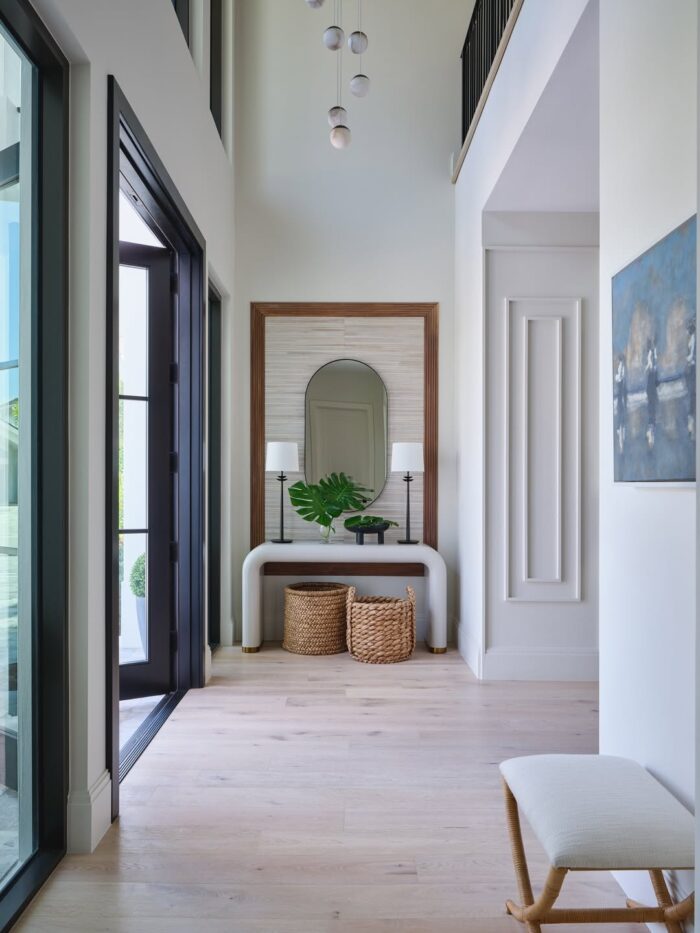 Light-filled entryway with tall ceilings, an arched mirror, sculptural white console table, woven baskets, and a multi-globe pendant light.
