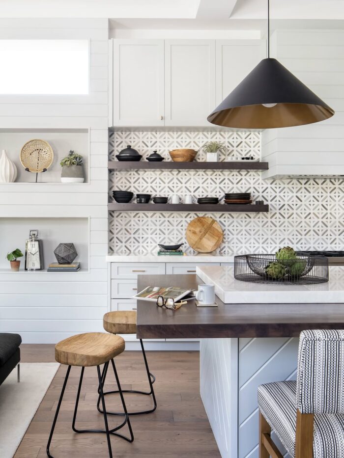 Contemporary kitchen with patterned tile backsplash, open shelving, wood barstools, and modern black pendant lighting.