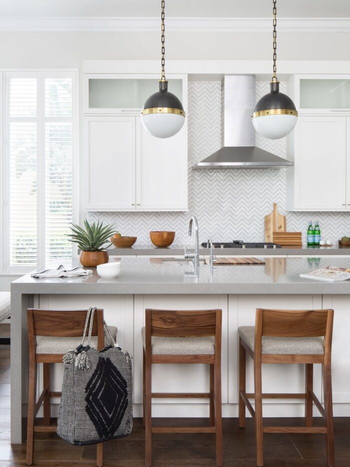 Coastal modern kitchen with white shaker cabinets, large island, natural wood barstools, and sculptural pendant lighting.
