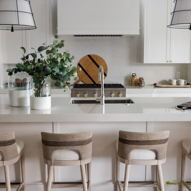 Bright coastal kitchen with a white island, woven-back barstools, large lantern-style pendant lights, and a white range hood in a modern Palm Beach design.