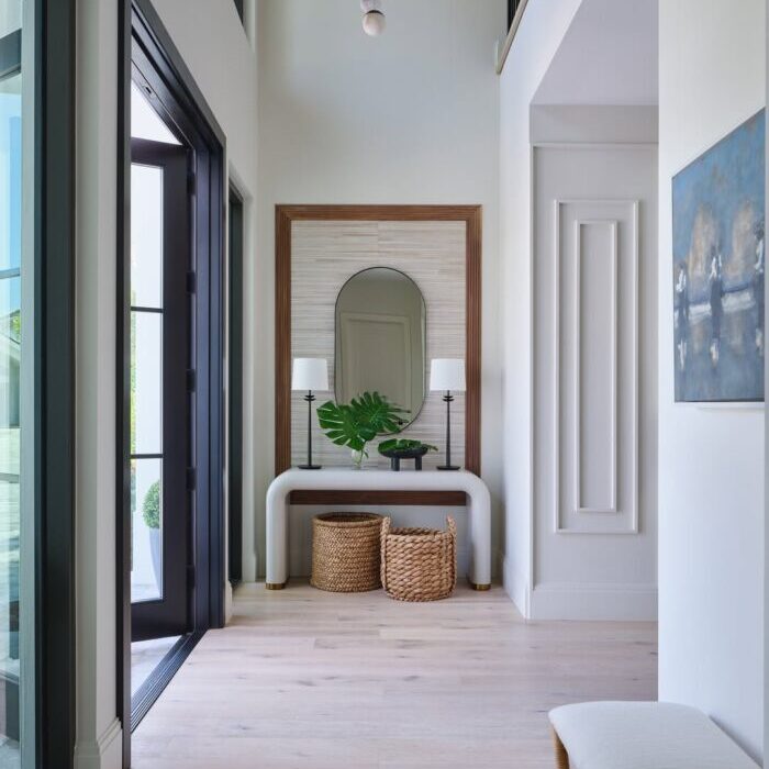Light-filled entryway with tall ceilings, an arched mirror, sculptural white console table, woven baskets, and a multi-globe pendant light.